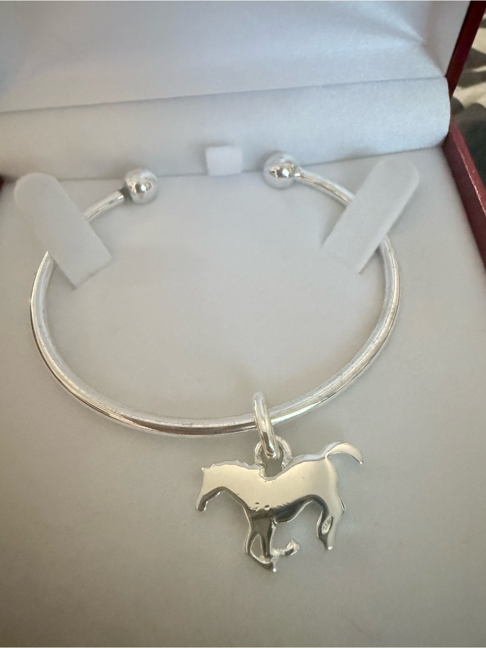 Silver bangle bracelet featuring a running horse charm.